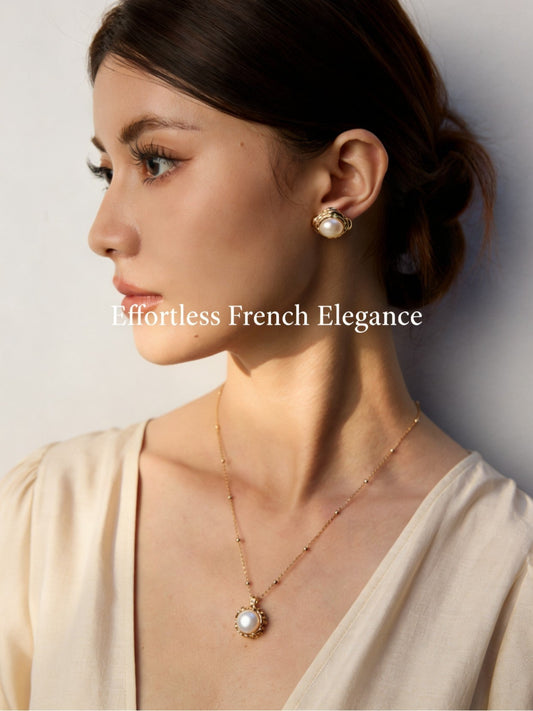 Close-up shot of an artisanal hammered silver pearl stud earring held by a hand to show scale and metallic texture.