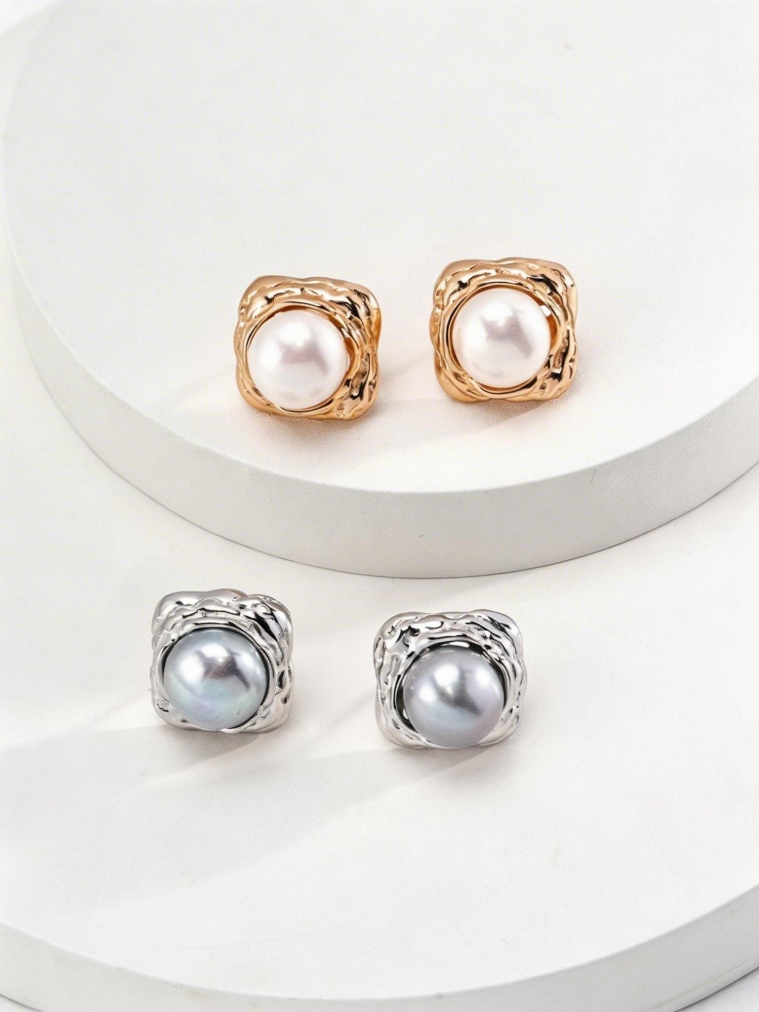 Pair of S925 Sterling Silver pearl stud earrings in Vintage Gold and White Gold finishes displayed on a white stone base.